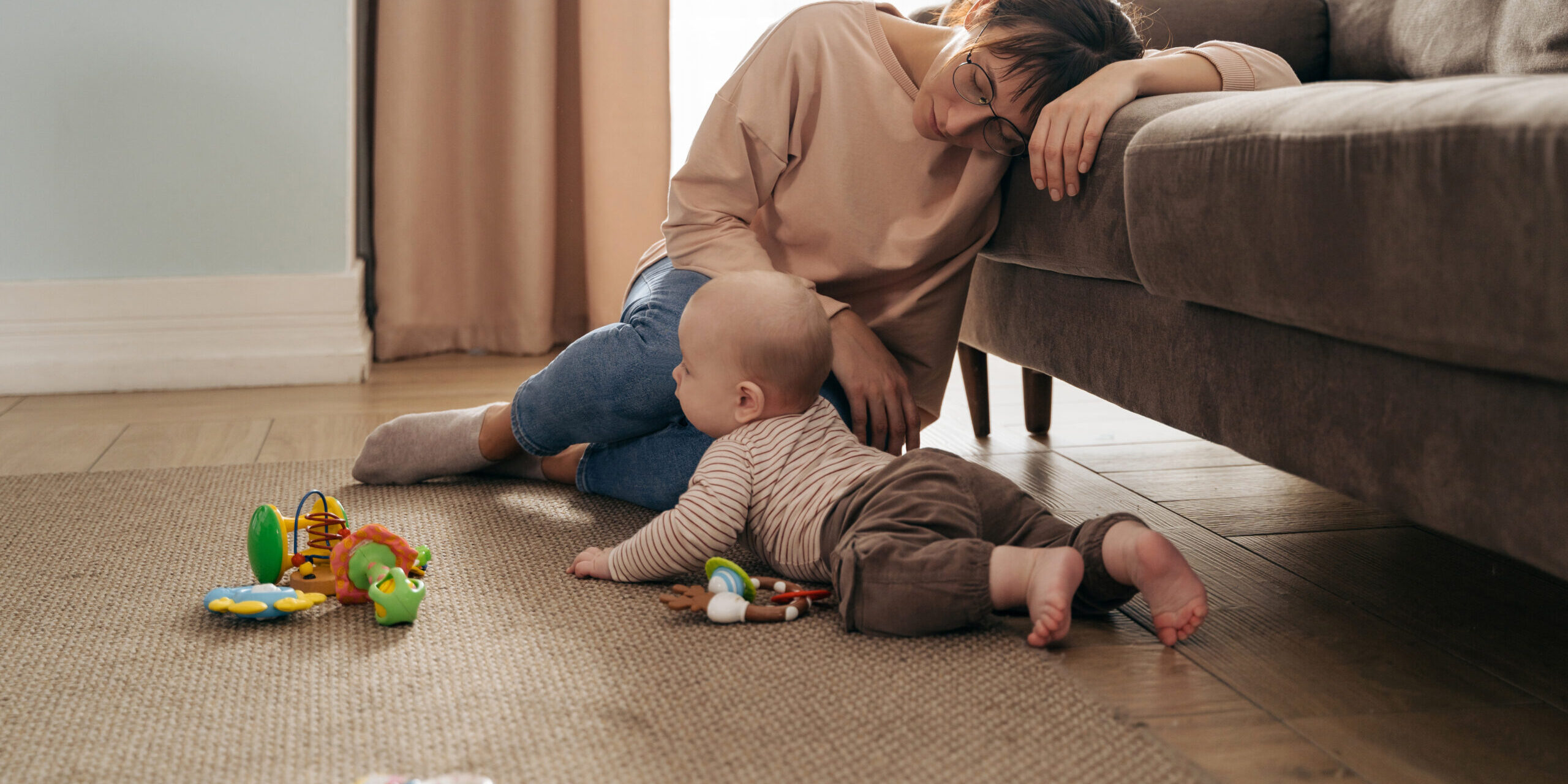 Young exhausted mother is very tired, fell asleep on sofa near her playing infant baby, suffering from postpartum depression, difficulties of motherhood, sleepless nights.
Mom's trying to take a nap